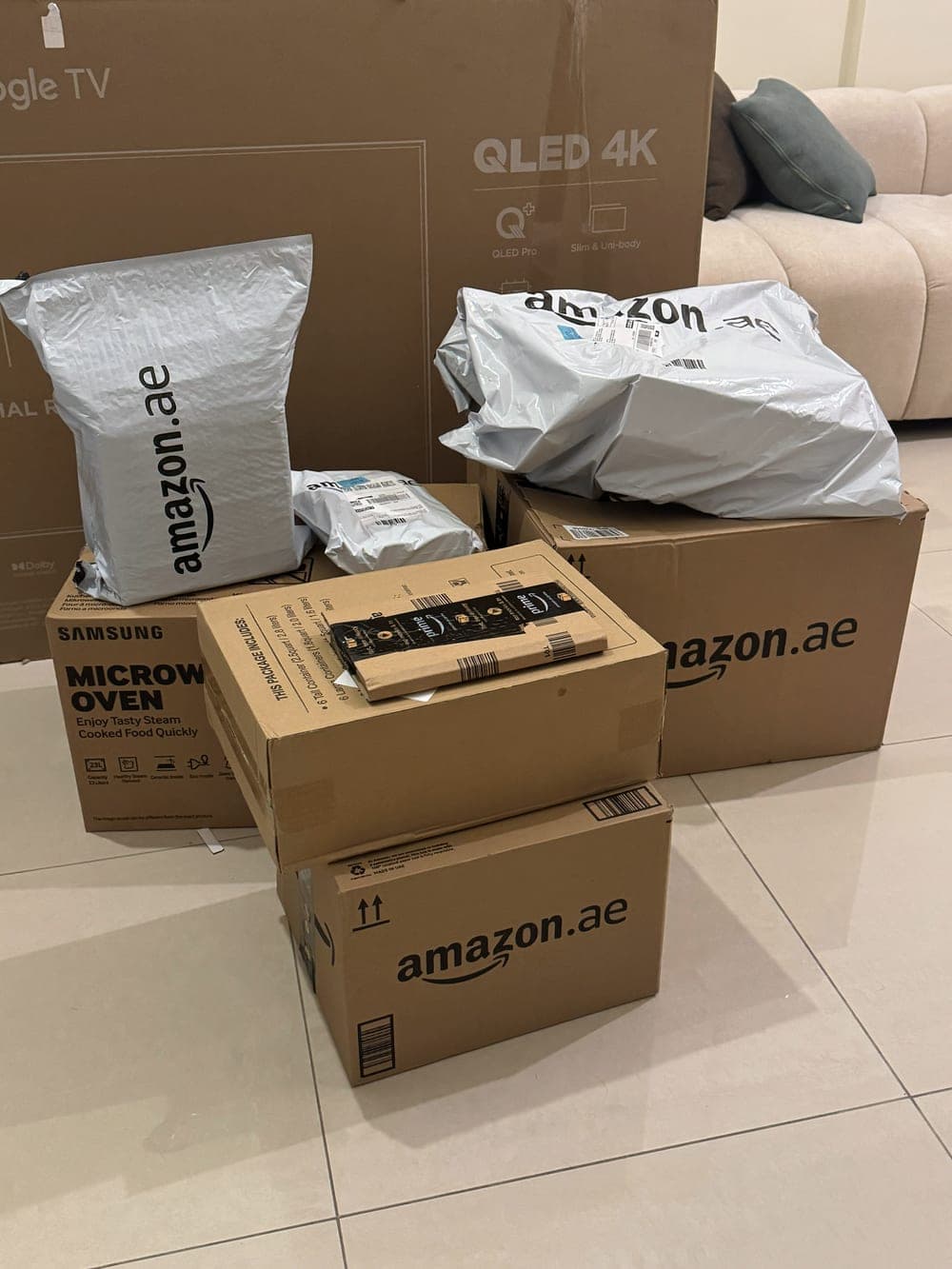 Amazon.ae parcels and a boxed microwave stacked on the tiled floor of an unfurnished apartment.